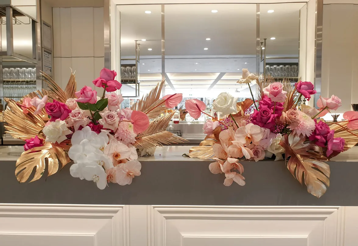 Pink and gold-leaf palm arrangements on a marble bar with a mirror behind