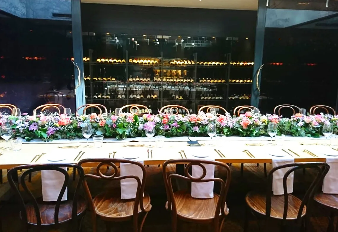 Pastel head-table garland in a lit wine-cellar wall setting with bentwood chairs