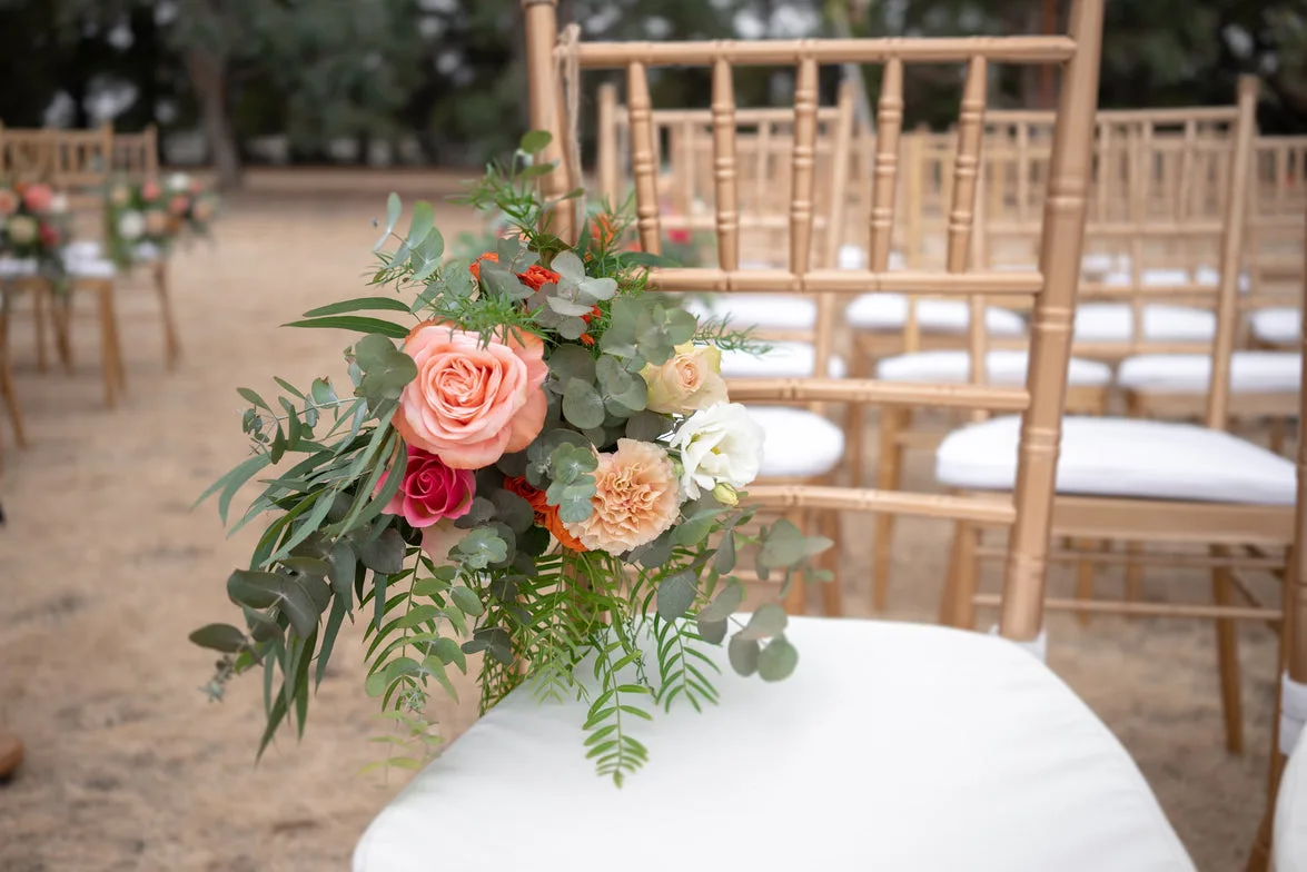 Single coral rose and eucalyptus posy resting on a gold chiavari chair