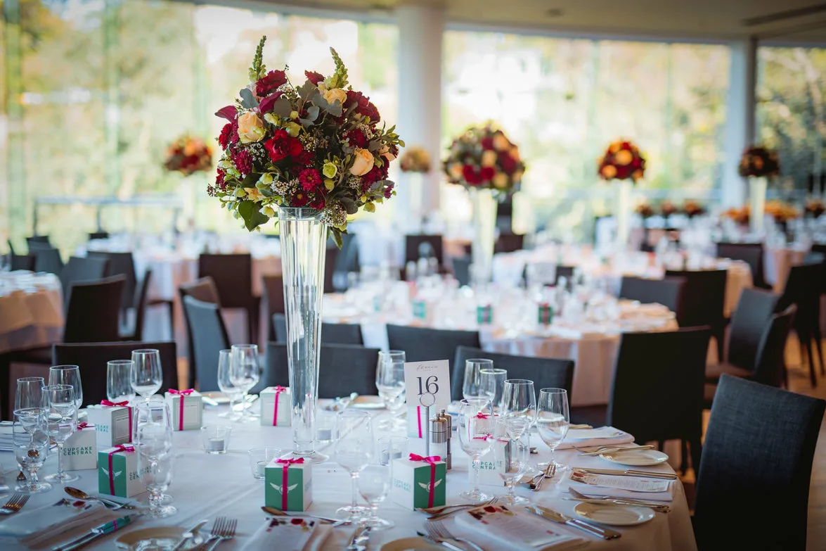 Tall vase with red and peach roses at a bright glass-walled reception