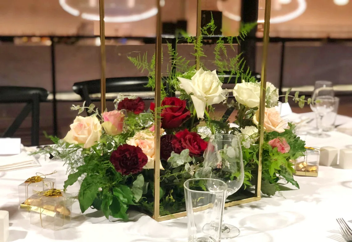 Low gold-frame centrepiece with red, white and blush roses on a white table