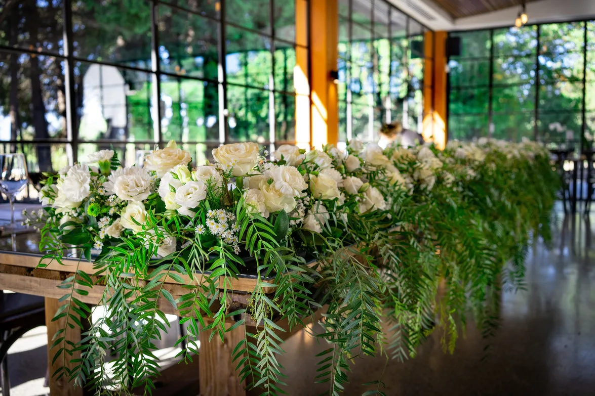 Long head-table garland with white roses in a glasshouse wedding venue
